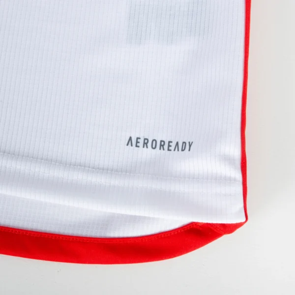 Close-up of the FC Bayern Munich Long Sleeve Home Jersey 23/24, in white with red trim on the sides. The fabric has a subtle vertical stripe texture, featuring AEROREADY near the hem to emphasize its moisture-wicking properties.