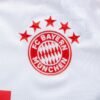 The image features the FC Bayern München logo on a white jersey, reminiscent of the FC Bayern Munich Home Jersey 23/24. The logo includes four red stars above a red circle with the clubs name and central diamond pattern.