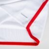 A close-up of a white fabric corner with red trim, similar to the FC Bayern Munich Home Jersey 23/24, shows a subtle ribbed texture and a small AEROREADY logo in black text.