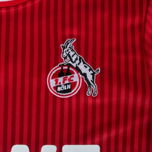 The FC Köln Away Jersey 23/24 features a vibrant red with vertical stripes, highlighted by the embroidered 1. FC Köln logo—a goat over a circular 1. FC KÖLN emblem.