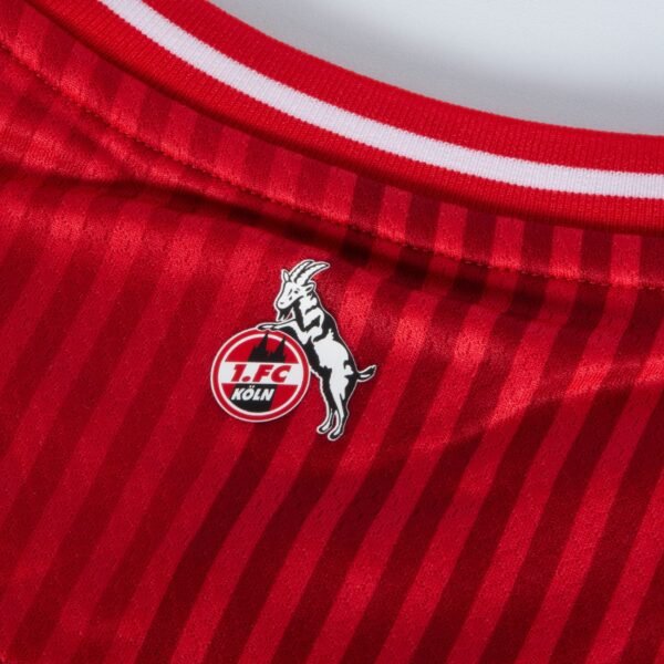 Close-up of the FC Köln Away Jersey 23/24: a red striped design with the iconic logo of a goat over a circular 1. FC Köln emblem in bold red and white, finished with a sleek white-trimmed collar.
