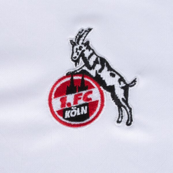 The white FC Köln Home Jersey 23/24 features an embroidered logo of a black and white goat on a red circle, with 1. FC KÖLN text and cathedral spires imagery.