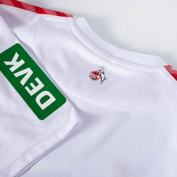 The FC Köln Home Jersey 23/24 is white with red accents. It features a green patch with DEK and has a goat-on-ball emblem near the collar, alongside a red circular logo.