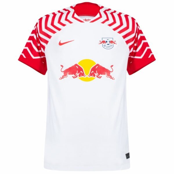 The RB Leipzig Home Jersey 23/24 showcases a white design with bold red zigzag patterns on the shoulders and sleeves, featuring the iconic logo of two red bulls and a yellow sun. A small red Nike swoosh decorates the right side.