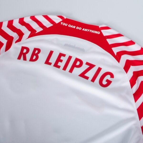 The RB Leipzig Home Jersey 23/24 features eye-catching red and white striped sleeves and the inspiring message YOU CAN DO ANYTHING on the upper back collar, blending style with a spirit of determination.