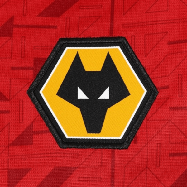 The Wolverhampton Away Jersey 23/24 showcases a vibrant red geometric pattern. Centrally, a hexagonal logo features a stylized black wolfs head on a yellow background outlined in black.