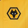 The Wolverhampton Home Jersey 23/24 features a close-up of its yellow fabric, showcasing a black and white hexagonal wolves logo with a stylized wolf head. The emblem is outlined in white and black, providing contrast against the vibrant background.