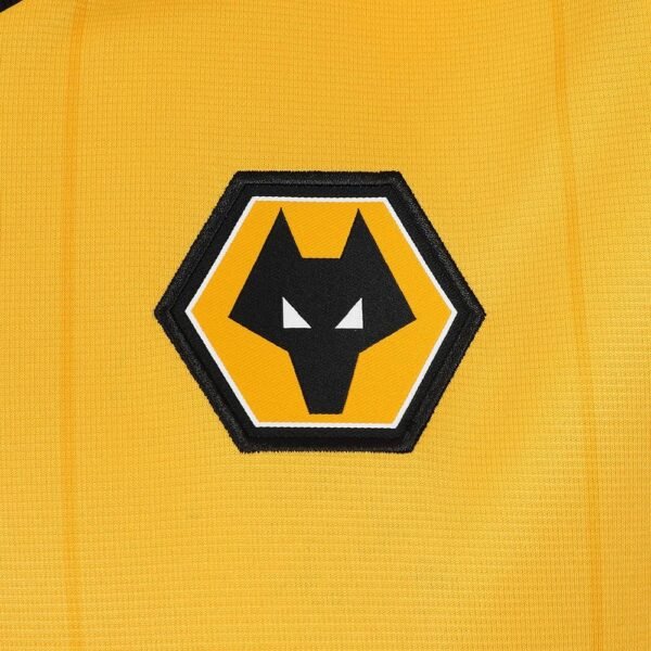 The Wolverhampton Home Jersey 23/24 features a close-up of its yellow fabric, showcasing a black and white hexagonal wolves logo with a stylized wolf head. The emblem is outlined in white and black, providing contrast against the vibrant background.